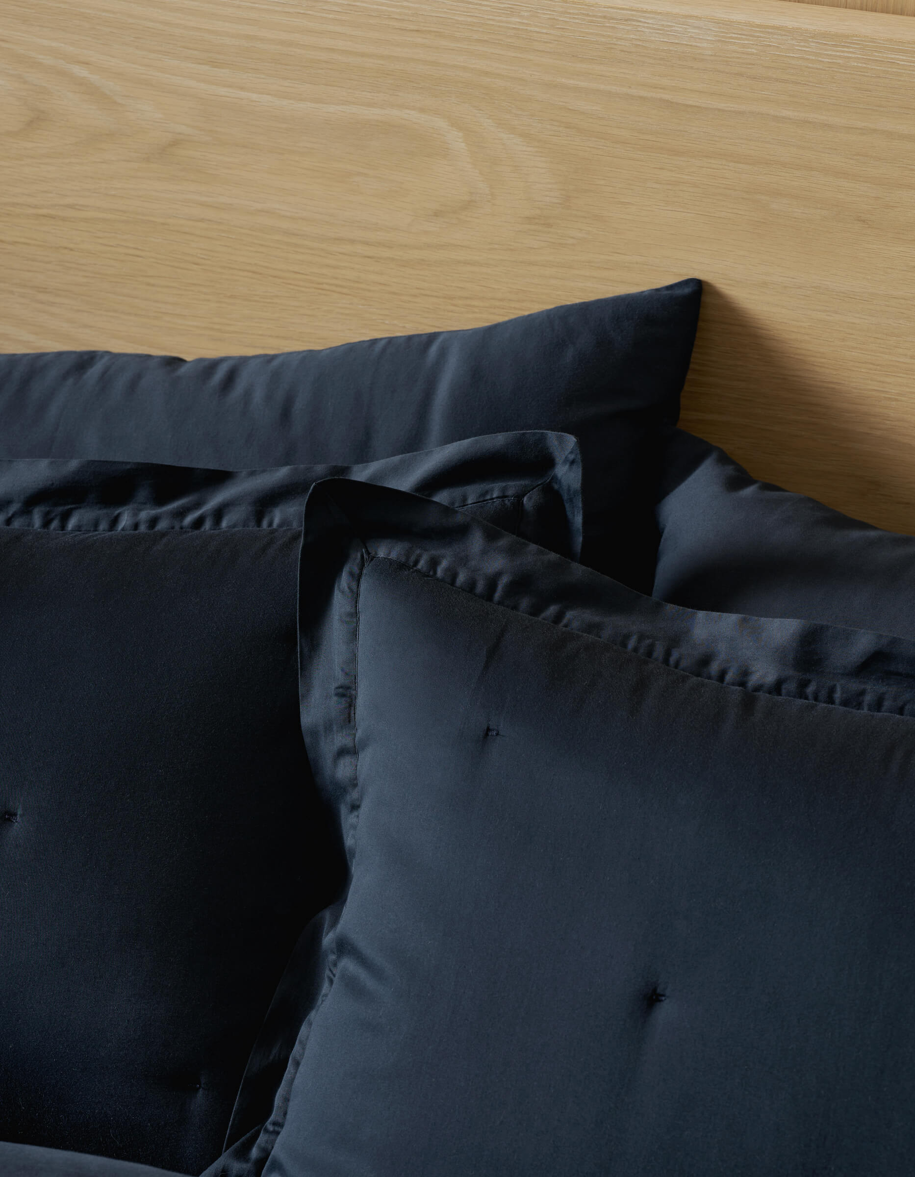 Two Soft-Wash Cotton Quilted Shams from Cozy Earth rest against a light wood headboard, with a black duvet partially visible in the foreground.