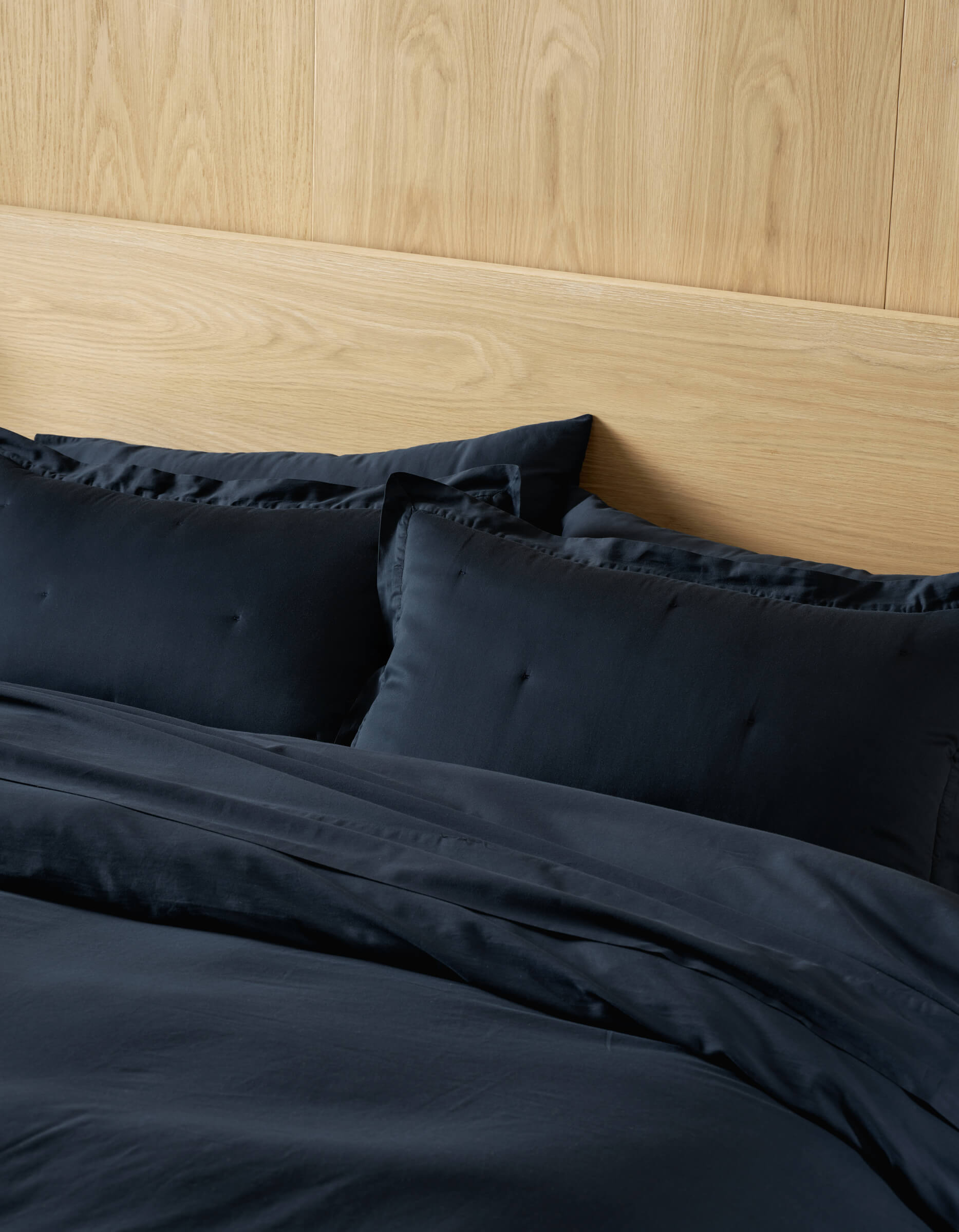 A neatly made bed featuring Cozy Earth Soft-Wash Cotton Quilted Shams in black, complemented by matching sheets and a comforter, set against a light wood headboard and wall.