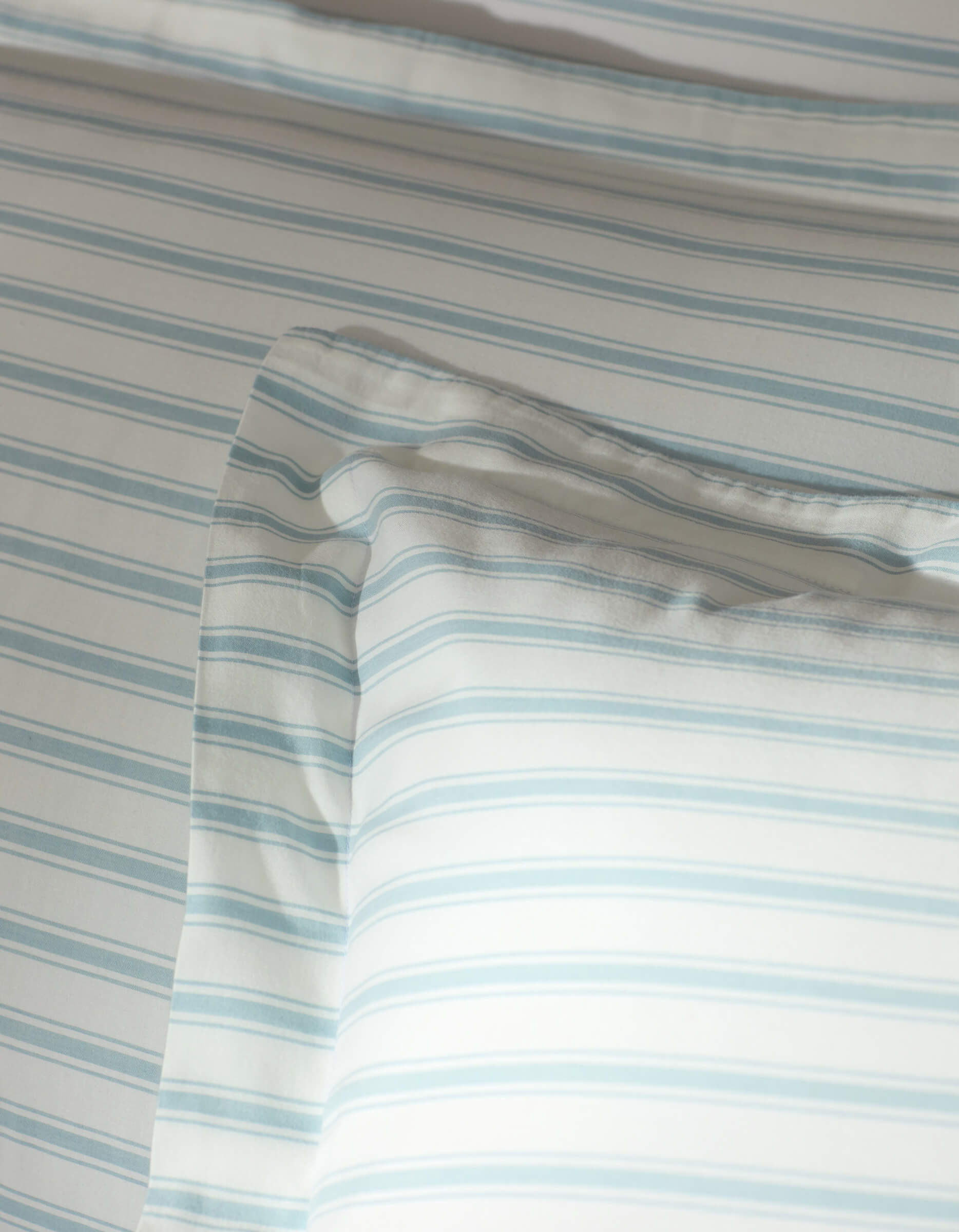 A close-up of a bed featuring Cozy Earth’s Soft-Wash Cotton Shams, dressed in white with thin, light blue stripes. The soft fabric and minimalist pattern create a calm, inviting look.