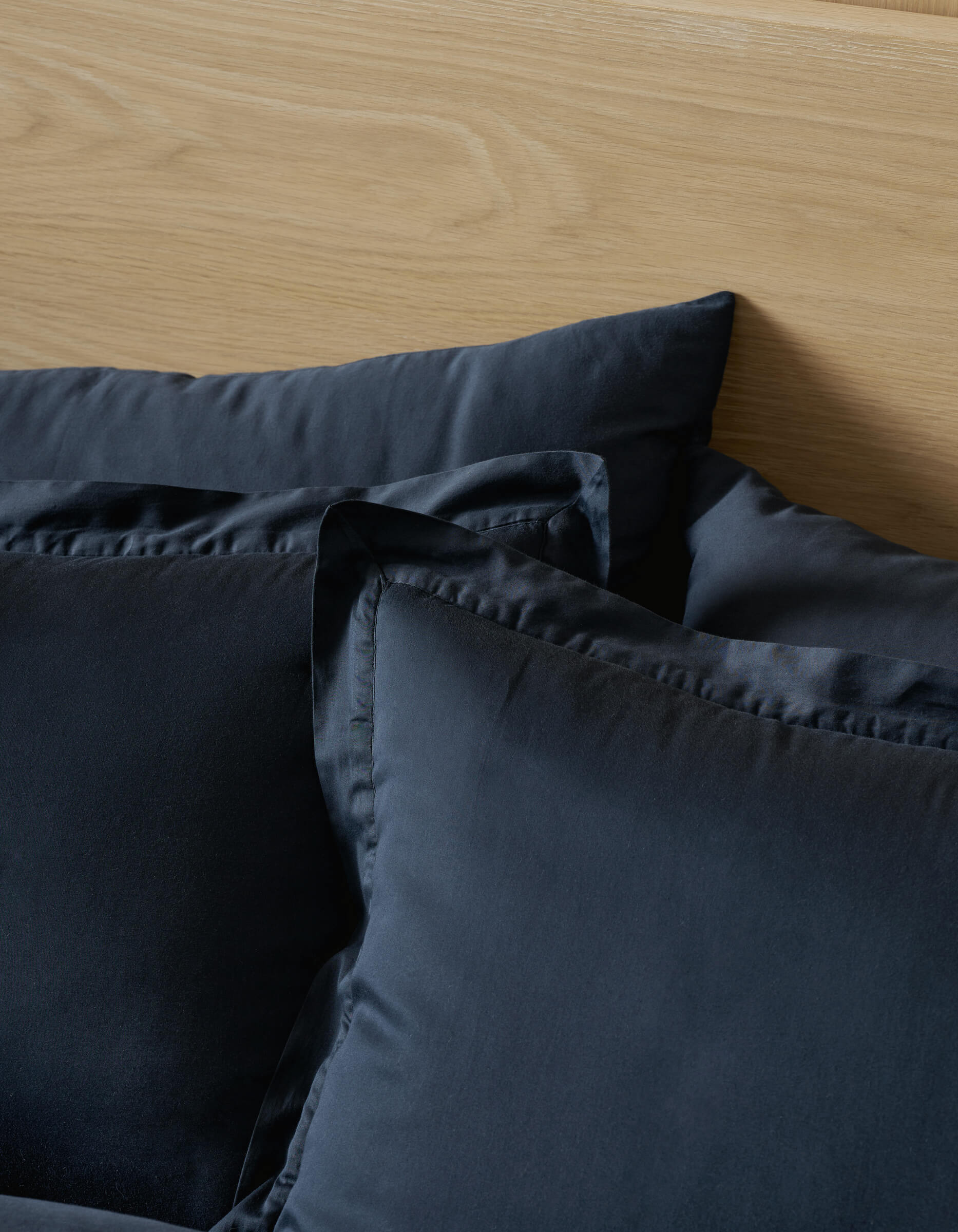 A close-up of a bed featuring a light wood headboard and two neatly arranged Cozy Earth Soft-Wash Cotton Shams in dark gray pillowcases.