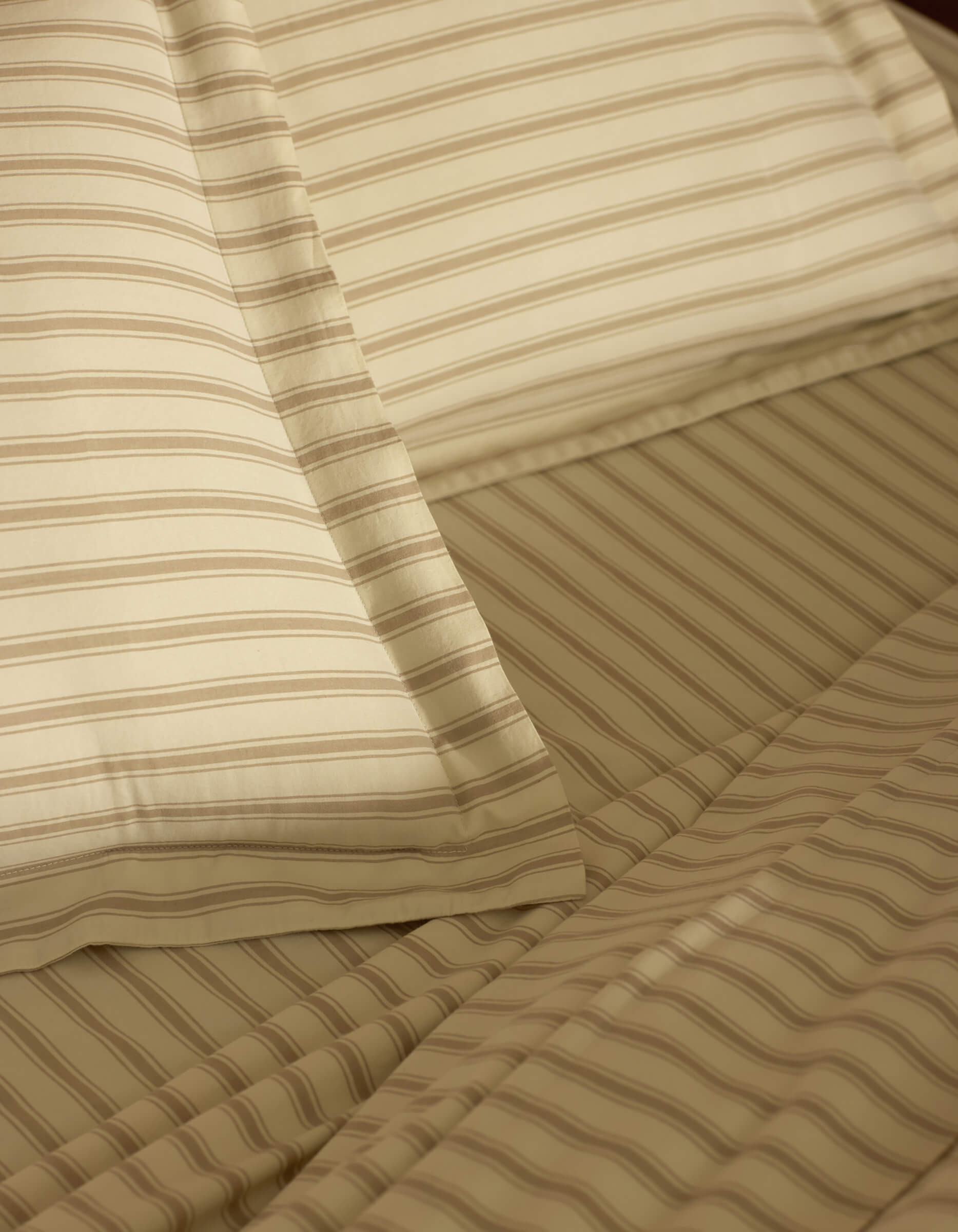 Close-up of a neatly made bed featuring Cozy Earth Soft-Wash Cotton Shams in beige and light brown stripes, highlighting the fabric's texture and precise alignment.
