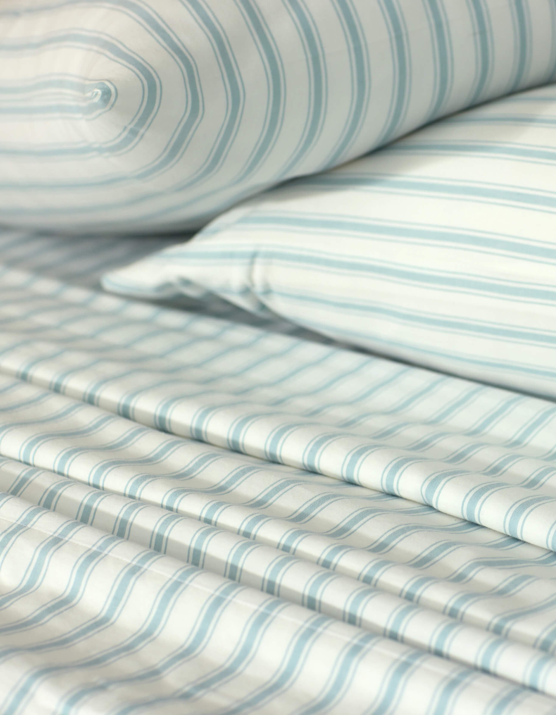 Close-up of a neatly made bed showcasing the Cozy Earth Soft-Wash Cotton Sheet Set, including a pillow, fitted sheet, and flat sheet in a light blue and white striped pattern. The smooth fabric looks exceptionally soft.