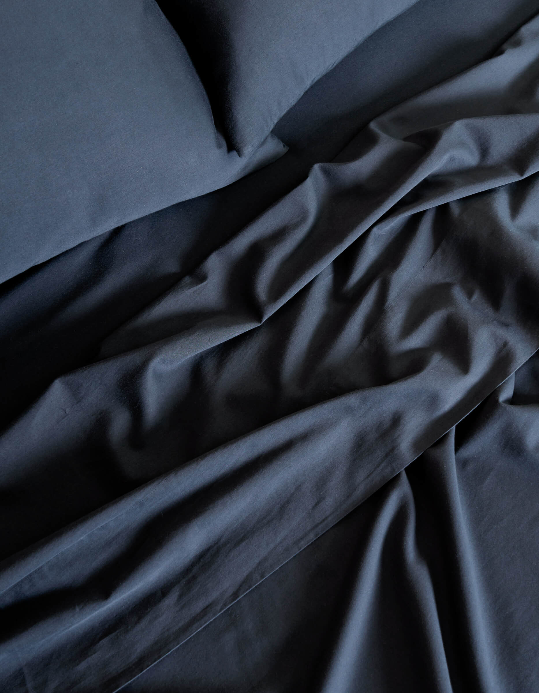 A close-up of the Cozy Earth Soft-Wash Cotton Sheet Set in dark blue highlights the soft folds and creases in the fabric on the bed.