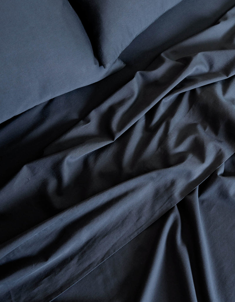 A close-up of the Cozy Earth Soft-Wash Cotton Sheet Set in dark blue highlights the soft folds and creases in the fabric on the bed.