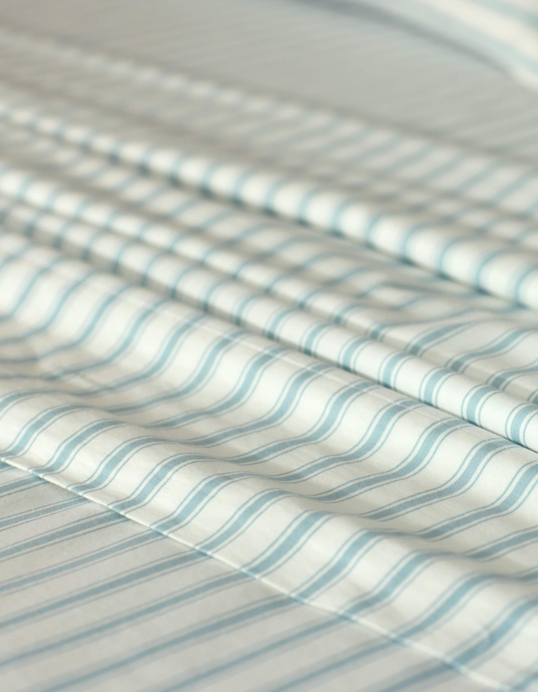 Close-up of the Cozy Earth Soft-Wash Cotton Flat Sheet in white with light blue horizontal stripes, displaying gentle folds and a textured, airy look.