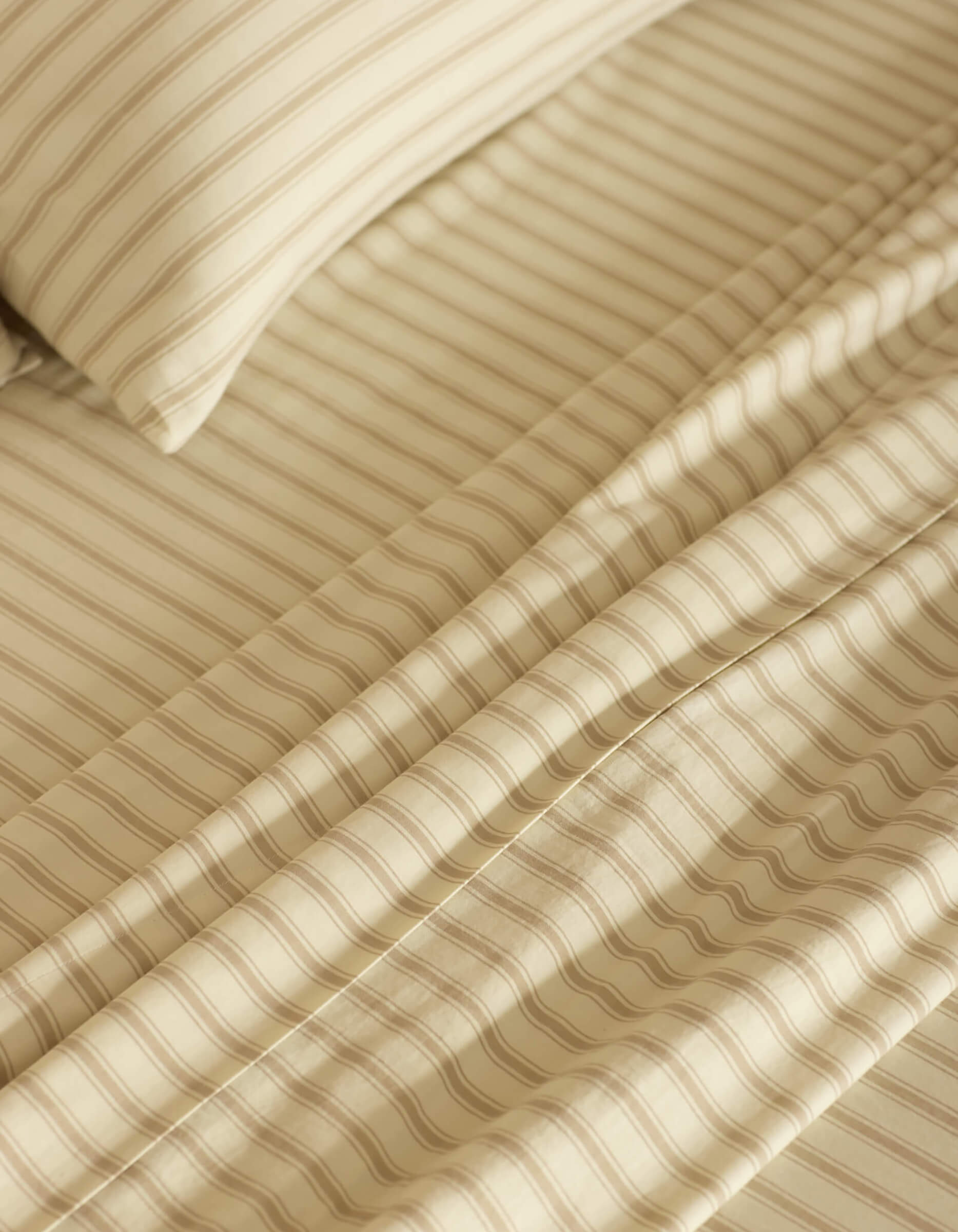 Close-up of a neatly made bed featuring the Cozy Earth Soft-Wash Cotton Sheet Set in beige and cream stripes. The smooth fabric and evenly spaced stripes create a calm, cozy atmosphere.