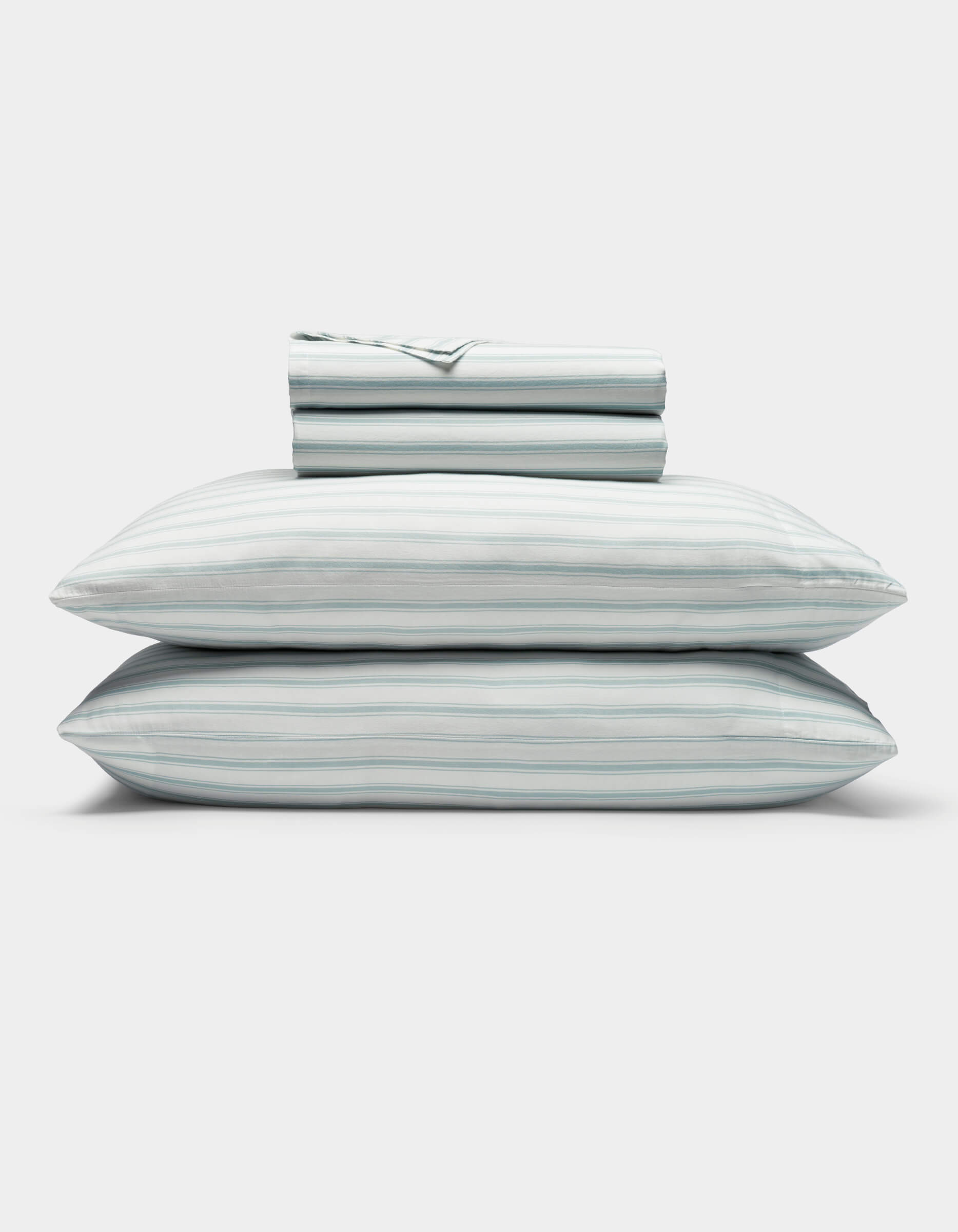 A neatly folded Soft-Wash Cotton Sheet Set by Cozy Earth in light blue and white stripes, featuring two stacked pillows and a folded fitted sheet, displayed on a plain white background.