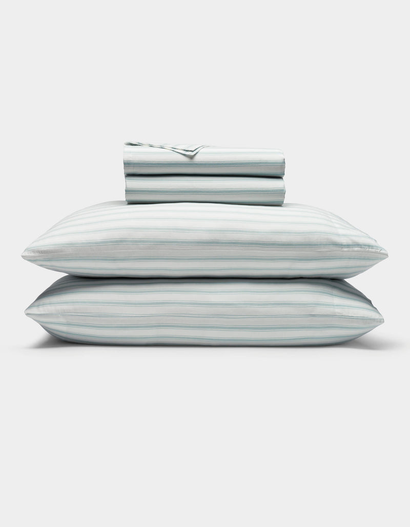 A neatly folded Soft-Wash Cotton Sheet Set by Cozy Earth in light blue and white stripes, featuring two stacked pillows and a folded fitted sheet, displayed on a plain white background.
