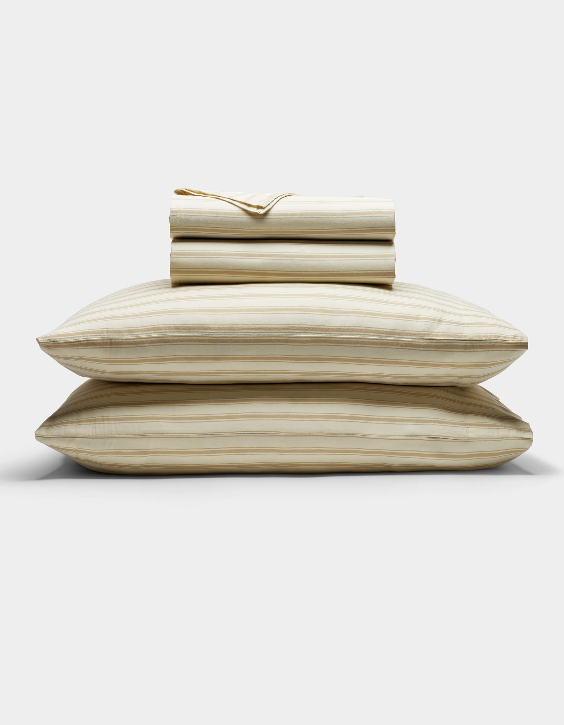 The Cozy Earth Soft-Wash Cotton Sheet Set in beige and light brown stripes is neatly stacked with two pillows at the base, topped with folded sheets and a pillowcase, displayed against a plain white background.