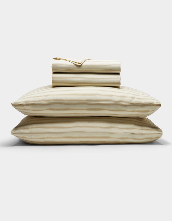 The Cozy Earth Soft-Wash Cotton Sheet Set in beige and light brown stripes is neatly stacked with two pillows at the base, topped with folded sheets and a pillowcase, displayed against a plain white background.|Color:Coconut and Sandalwood Stripe