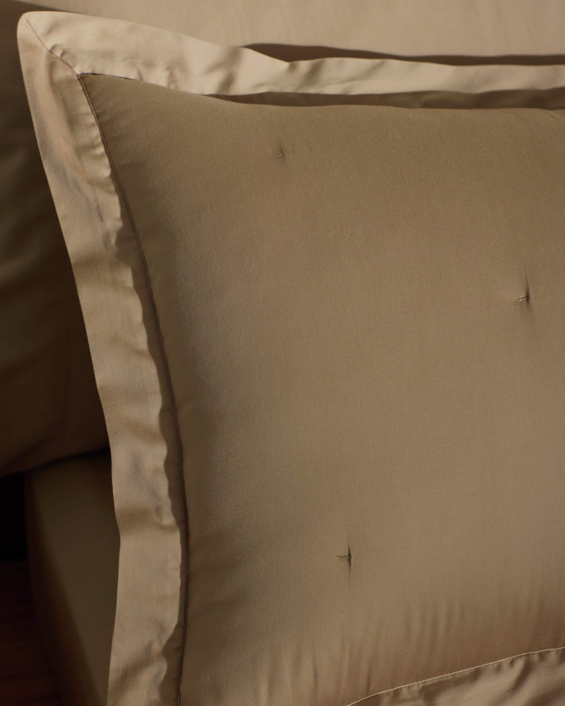A close-up of a neatly made bed featuring Cozy Earth Soft-Wash Cotton Quilted Shams in beige, showcasing their smooth quilted texture and subtle tufting, complemented by matching beige bedding.