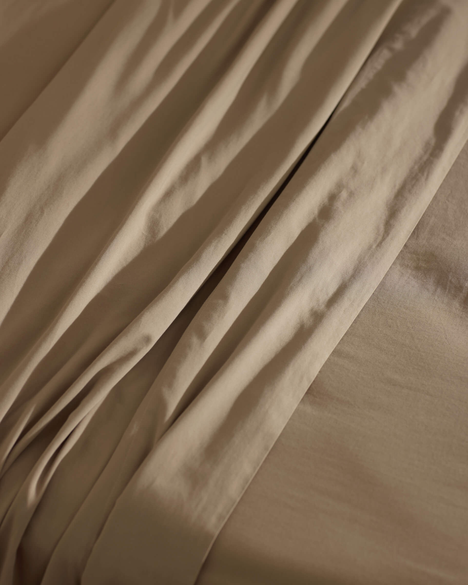Close-up of Cozy Earth’s Soft-Wash Cotton Sheet Set in beige, highlighting its gentle folds, subtle shadows, and smooth, cozy texture.