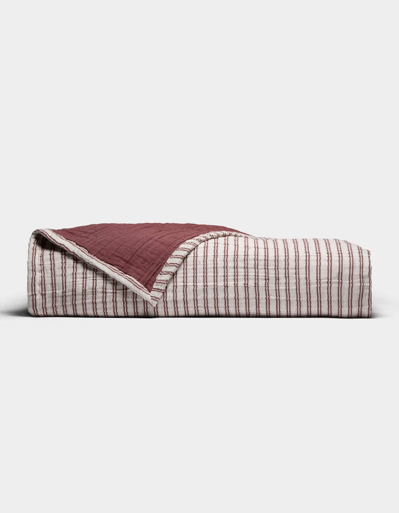 The Cozy Earth Waterfront Coverlet, a folded quilt in red and white stripes with one corner flipped to reveal a solid dark red underside, is displayed against a plain white background.