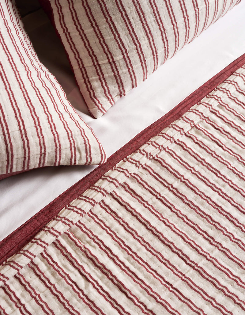Close-up of a bed dressed in the Cozy Earth Waterfront Coverlet Bundle, featuring white fabric with red vertical stripes and a solid red border for a coordinated, cozy look.