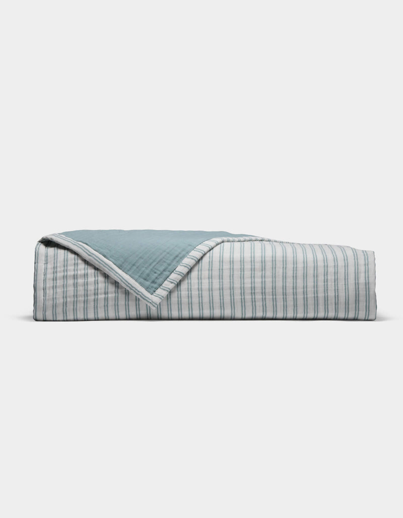 The Cozy Earth Waterfront Coverlet is a neatly folded quilt with a blue top and a white underside featuring thin blue stripes, displayed against a plain white background.