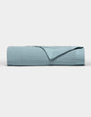 The Cozy Earth Waterfront Grid Matelasse Blanket in light blue is neatly folded against a plain white background, with the top layer turned back to show the inner fabric.|Color:River