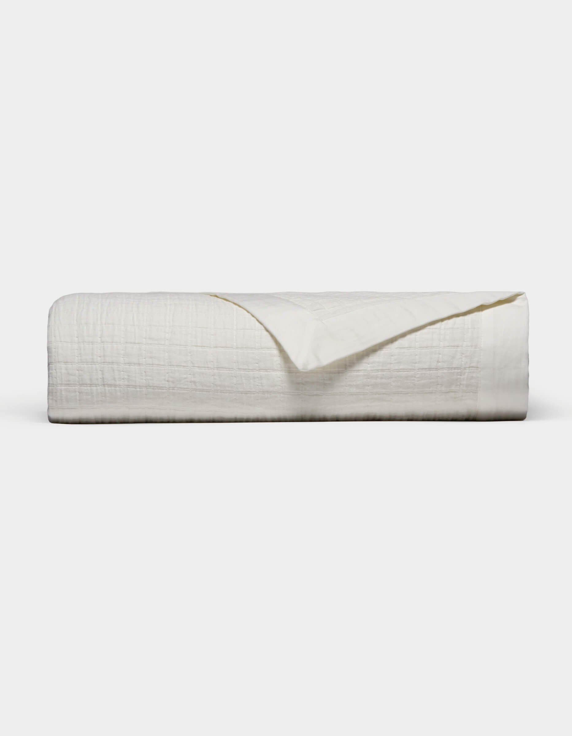 The Waterfront Grid Matelasse Blanket by Cozy Earth is shown neatly folded with a textured, crinkled surface against a plain light background. One corner is flipped over to reveal the underside.