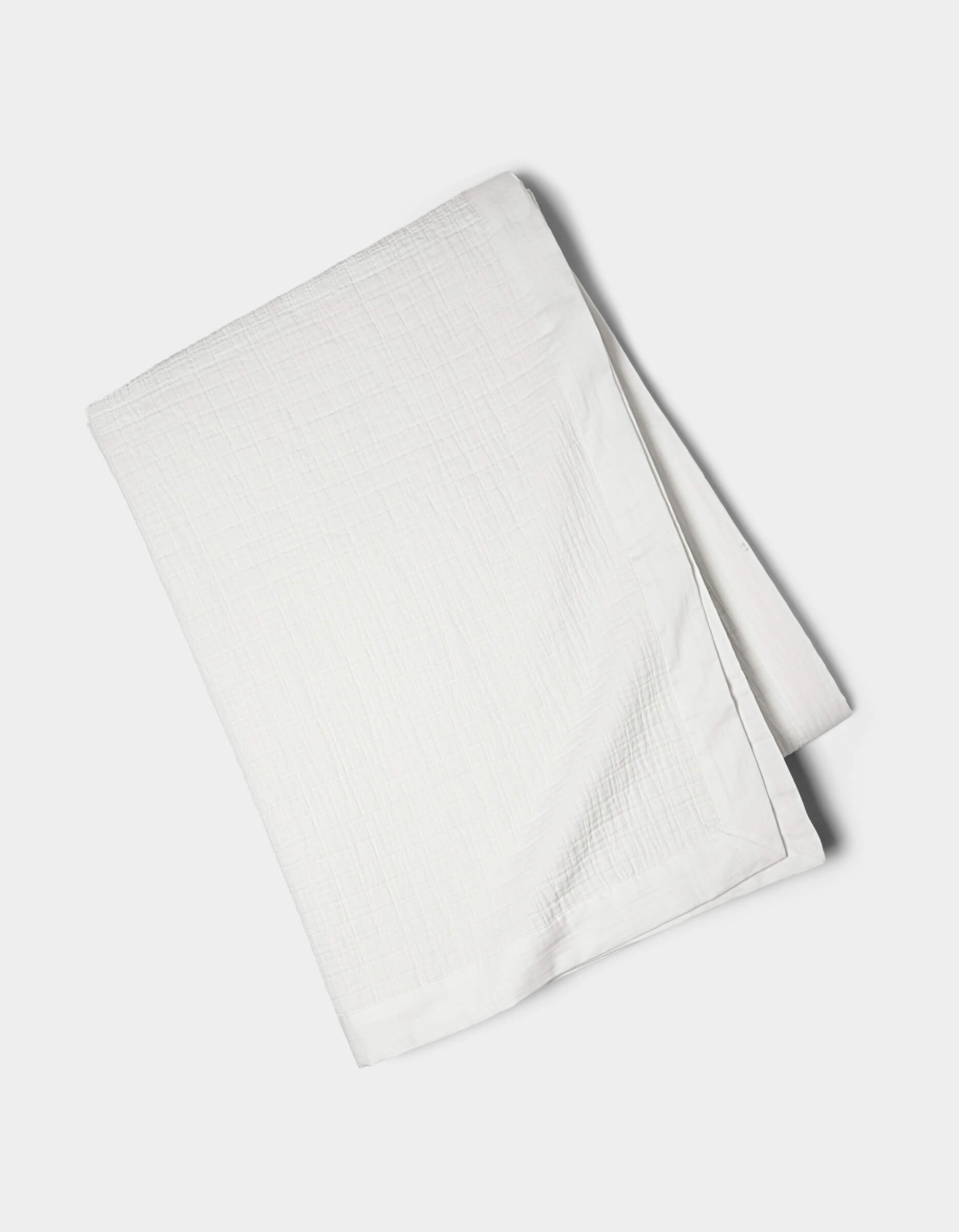 The Cozy Earth Waterfront Grid Matelasse Blanket, in white with a textured design, is neatly folded on a plain, light-colored surface.