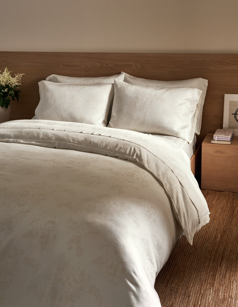 A neatly made bed with white bedding and matching pillows, set against a warm wood headboard in a softly lit bedroom. 