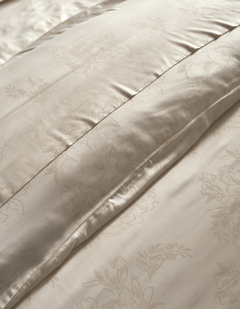 Close-up of a cream-colored satin duvet cover with a subtle floral damask pattern and stitched channel tufting.