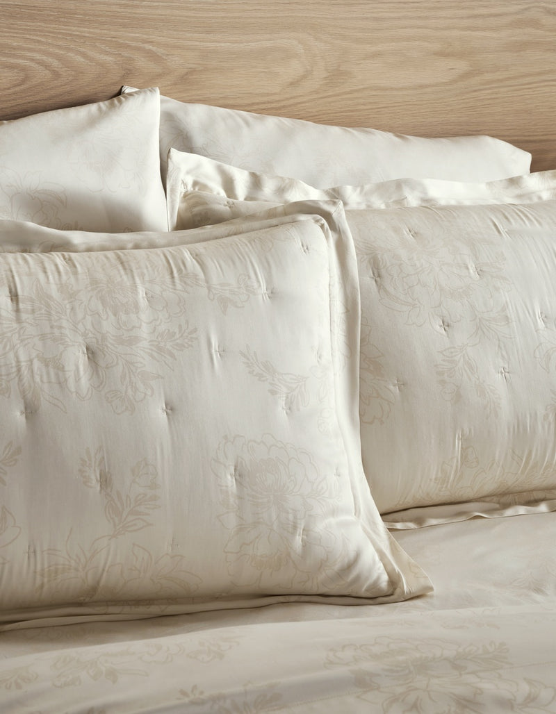 Cream-colored tufted and embroidered bedding set with matching pillows and a wooden headboard.