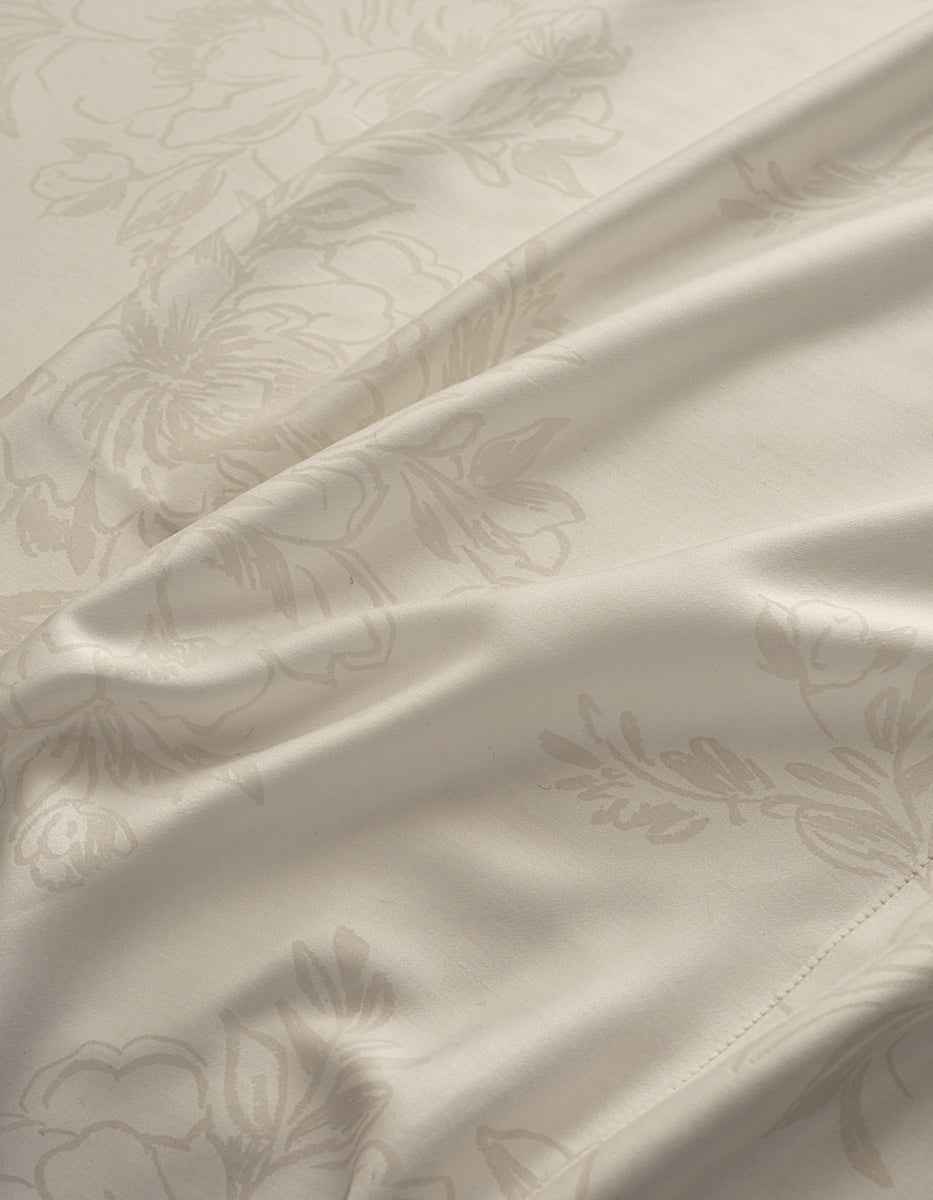 Close-up of a cream-colored satin fabric with a subtle, tonal damask floral pattern and soft folds. 