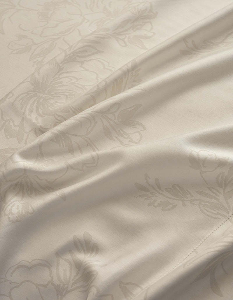 Close-up of a cream-colored satin fabric with a subtle, tonal damask floral pattern and soft folds.