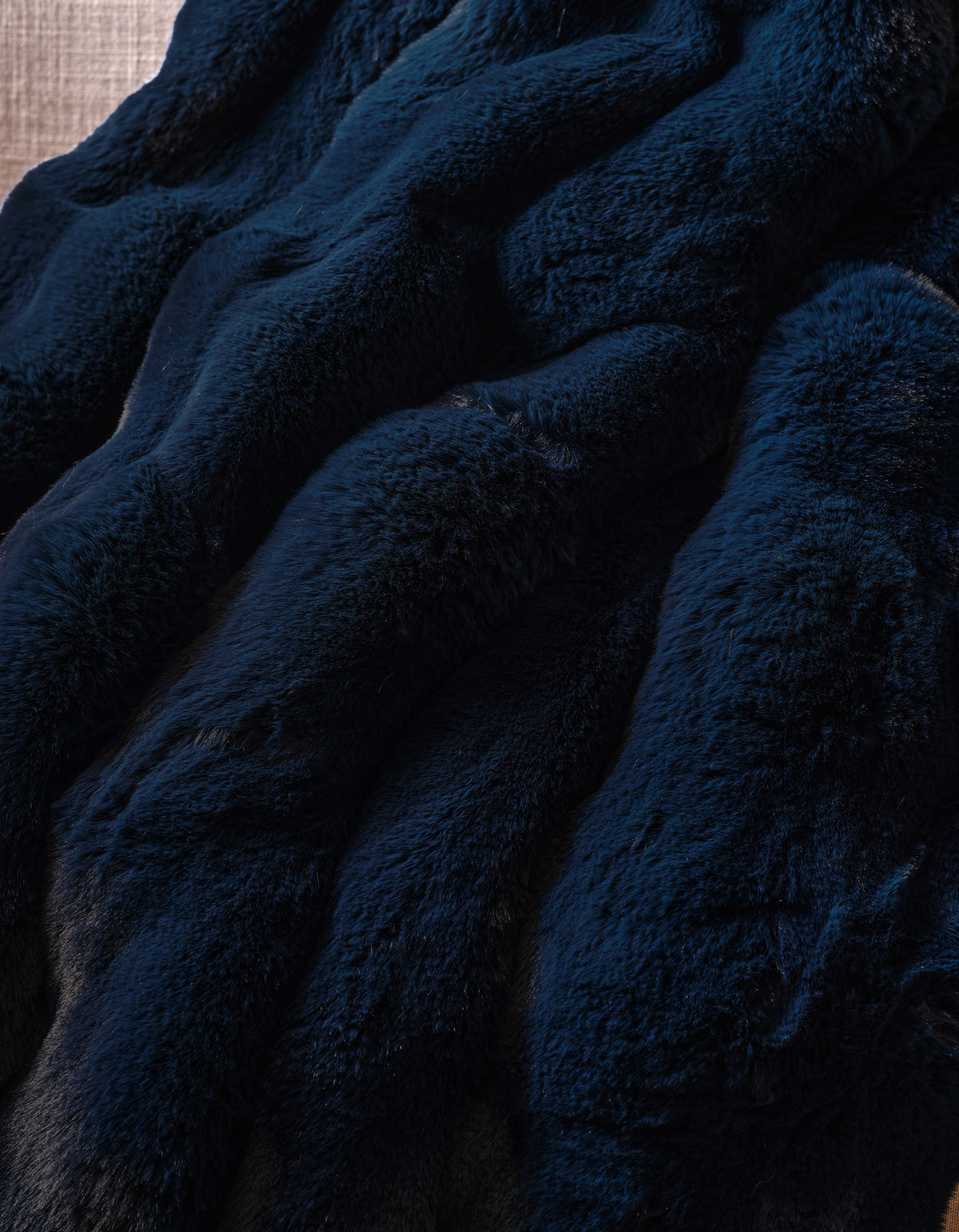 The Double Bubble Cuddle Blanket by Cozy Earth features dark blue faux fur fabric with a soft, plush texture, elegantly arranged in gentle, wavy folds.
