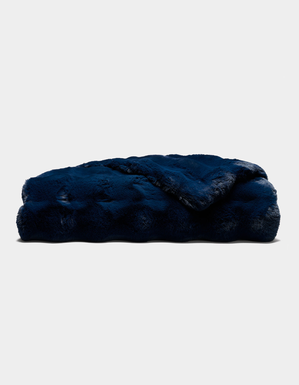 A folded Double Bubble Cuddle Blanket by Cozy Earth, in plush dark blue faux fur, rests on a plain light background. The blanket appears thick, soft, and cozy, featuring a slightly shiny texture.