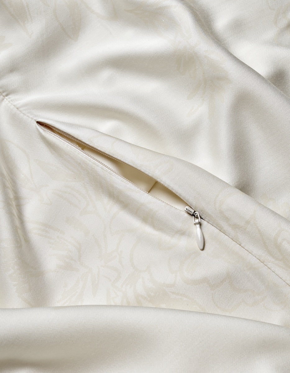 A close-up of the cream-colored Bamboo Duvet Cover by Cozy Earth highlights a partially open, concealed zipper pocket with a small pull tab, while subtle floral patterns enhance the satin-like fabric.