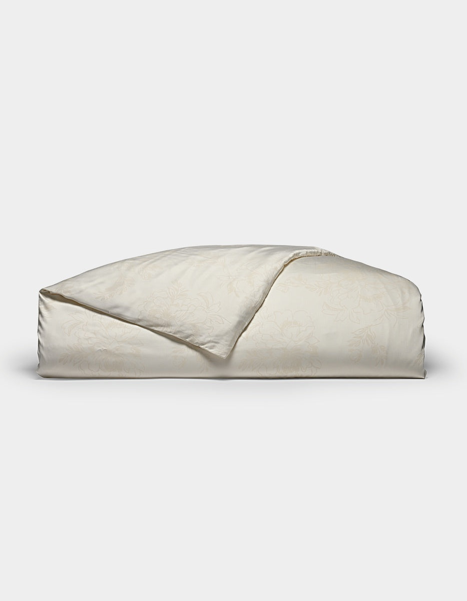 A folded Bamboo Duvet Cover by Cozy Earth in a light cream color with a subtle floral pattern is displayed on a plain white background.