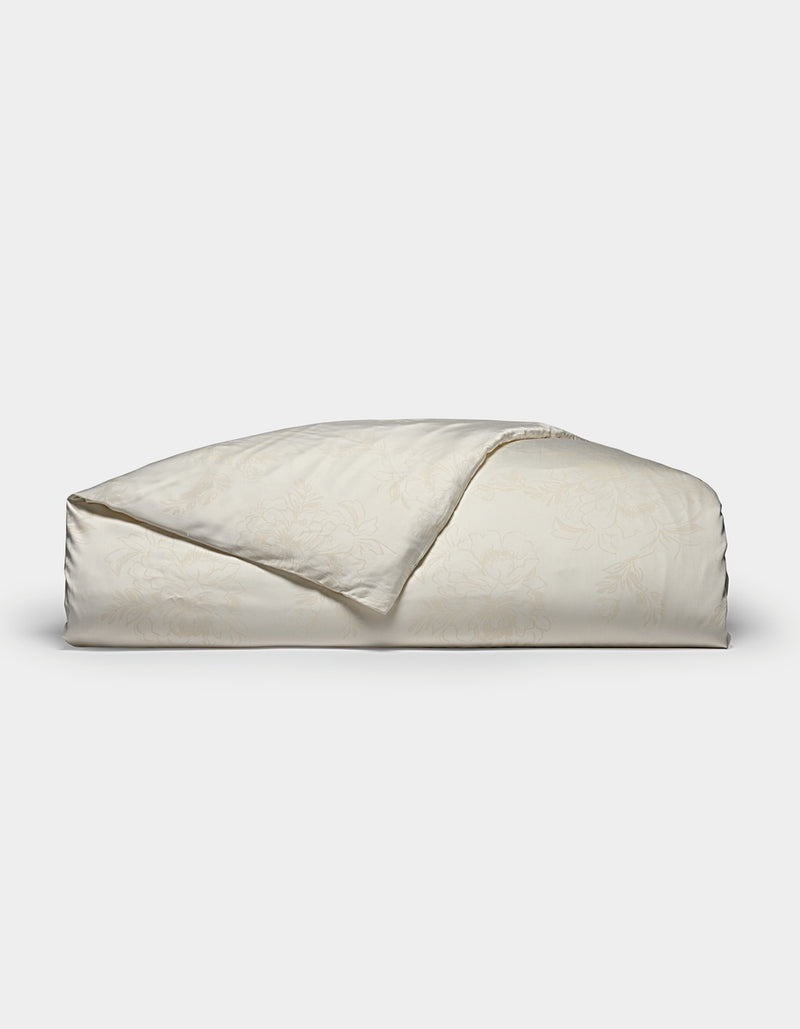A folded Bamboo Duvet Cover by Cozy Earth in a light cream color with a subtle floral pattern is displayed on a plain white background.