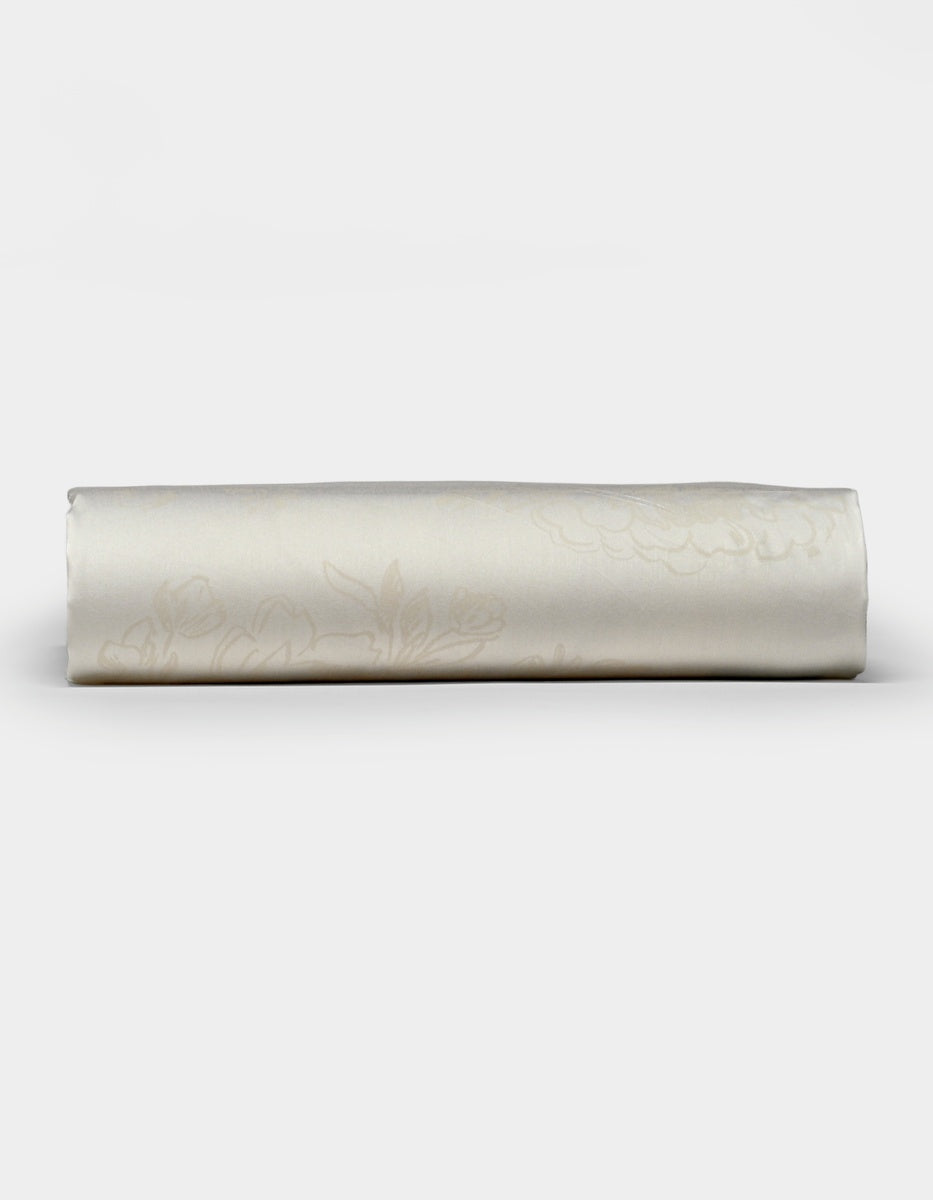 A neatly rolled Cozy Earth Bamboo Fitted Sheet in cream, featuring a subtle floral pattern, displayed on a plain white background.