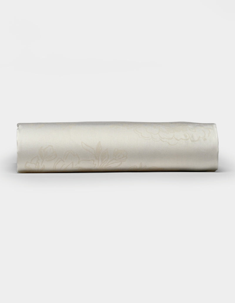 A neatly rolled Cozy Earth Bamboo Fitted Sheet in cream, featuring a subtle floral pattern, displayed on a plain white background.