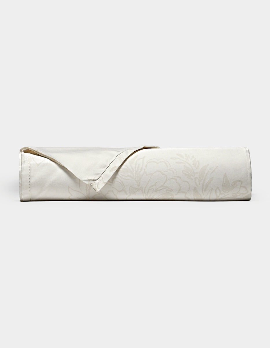 A neatly rolled Cozy Earth Bamboo Flat Sheet in cream, featuring a subtle floral pattern and a folded-back hemmed corner, displayed on a plain white background.