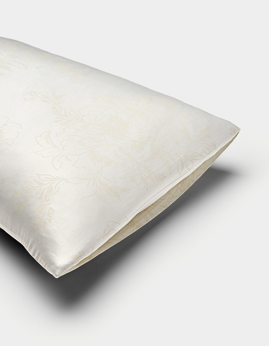 A close-up of a Cozy Earth Bamboo Pillowcase in cream, showing its envelope closure and subtle floral pattern on the satin-like fabric.