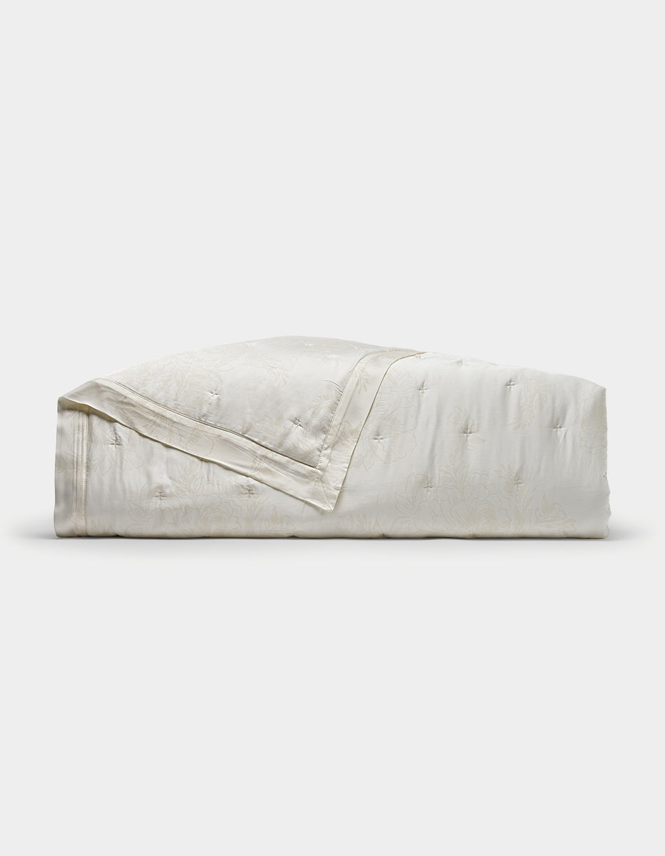 A folded Cozy Earth Bamboo Quilt in white, featuring a subtle floral pattern, displayed on a plain white background.|Color:Sonoma Floral in Vintage White