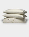 Two cream-colored pillows from the Cozy Earth Sonoma Stitch Quilt Bundle are stacked atop a matching folded blanket, all featuring a subtle checkered pattern, set against a plain white background.|Color:Vintage White