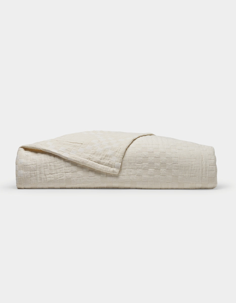 The Sonoma Stitch Quilt by Cozy Earth is a neatly folded, cream-colored quilt featuring a subtle checkered pattern and displayed on a plain white background.