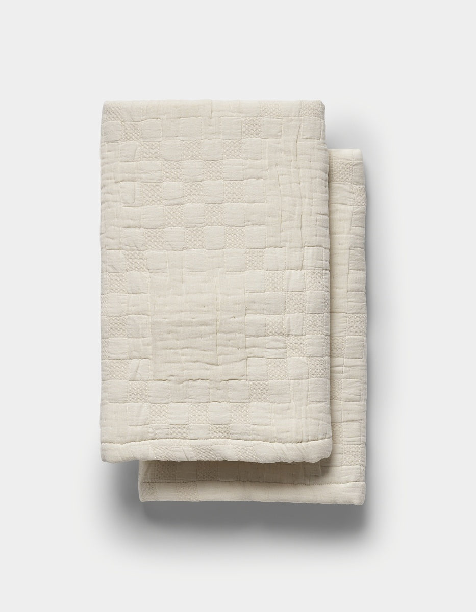 The Sonoma Stitch Shams by Cozy Earth, featuring a cream-colored fabric with a subtle textured checkered pattern, are neatly folded and displayed on a plain white background.