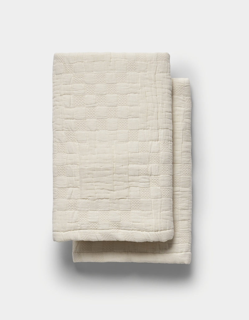 The Sonoma Stitch Shams by Cozy Earth, featuring a cream-colored fabric with a subtle textured checkered pattern, are neatly folded and displayed on a plain white background.