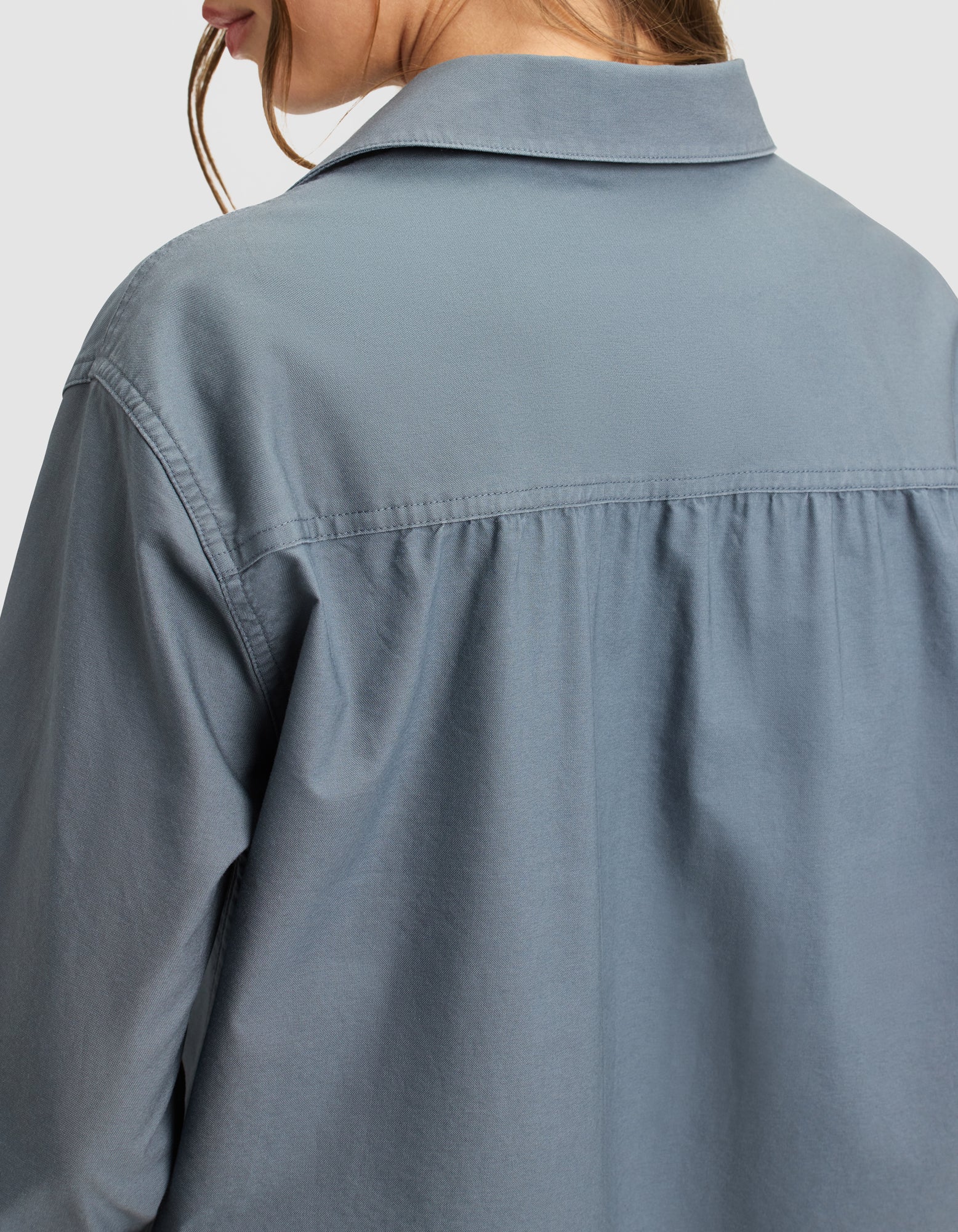 A close-up of a woman wearing the Cozy Earth Women's Camden Midi Dress, shown from the back and side, highlights the light blue fabric, collared neckline, visible yoke seam, and gentle gathers below the shoulders. 