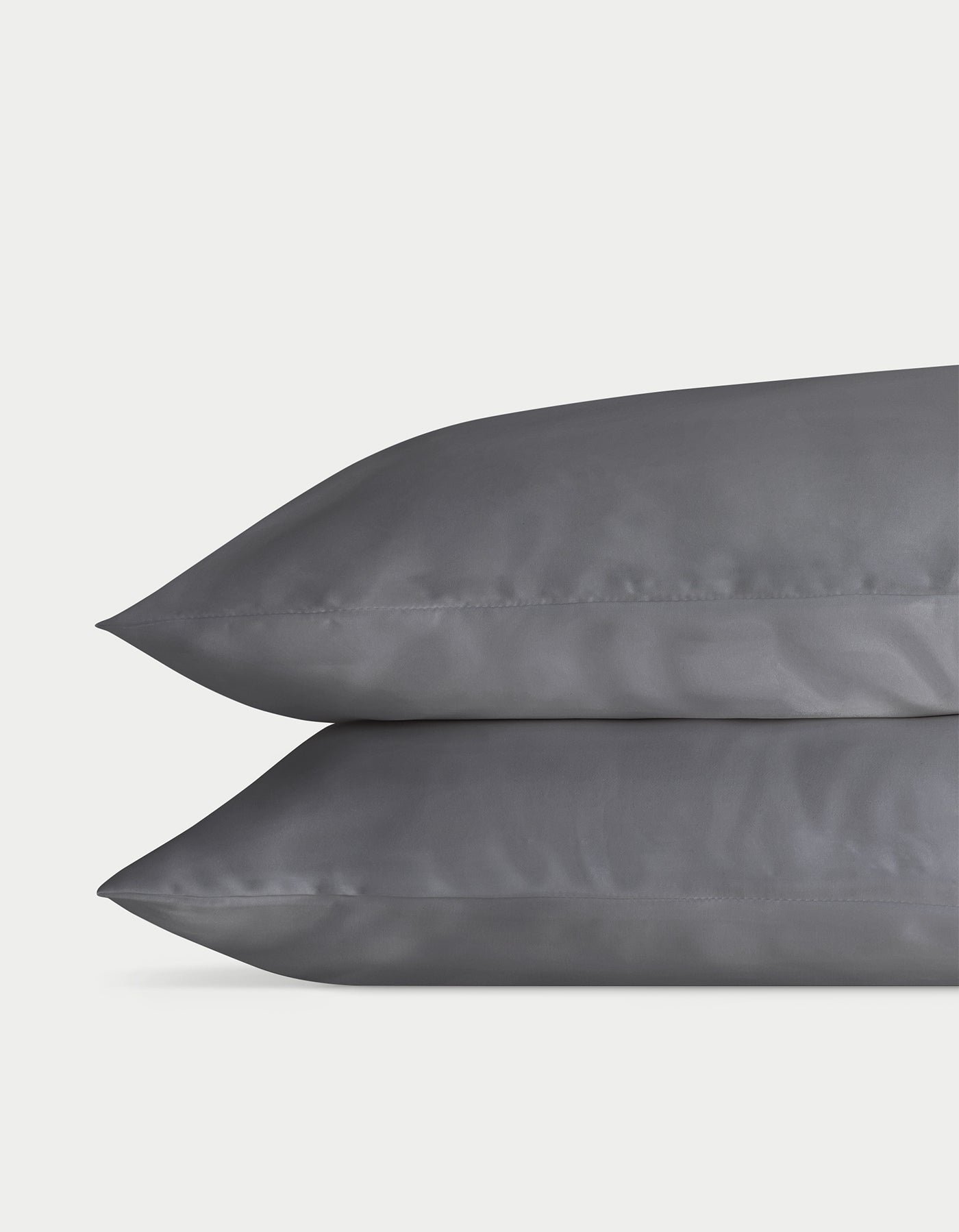 Against a plain light background, two stacked gray pillows from the Cozy Earth Bamboo Sheet Set showcase their silky, satin-like texture and reflective fabric. The neatly sewn edges enhance their plush and comfortable look. 