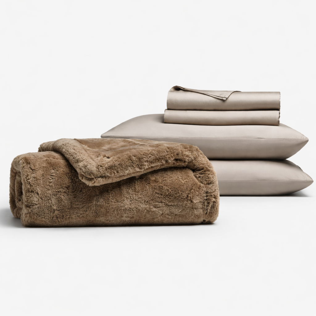 The Cozy Night In Bundle by Cozy Earth features a folded brown plush blanket, two stacked beige pillows, and a neatly folded beige sheet, all displayed against a white background.