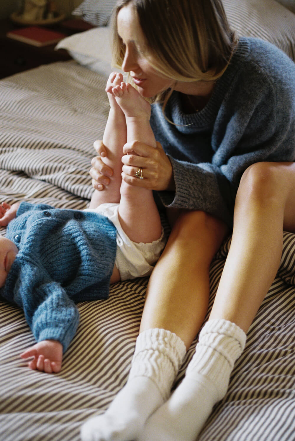 a woman kisses the feet of her baby on a bed