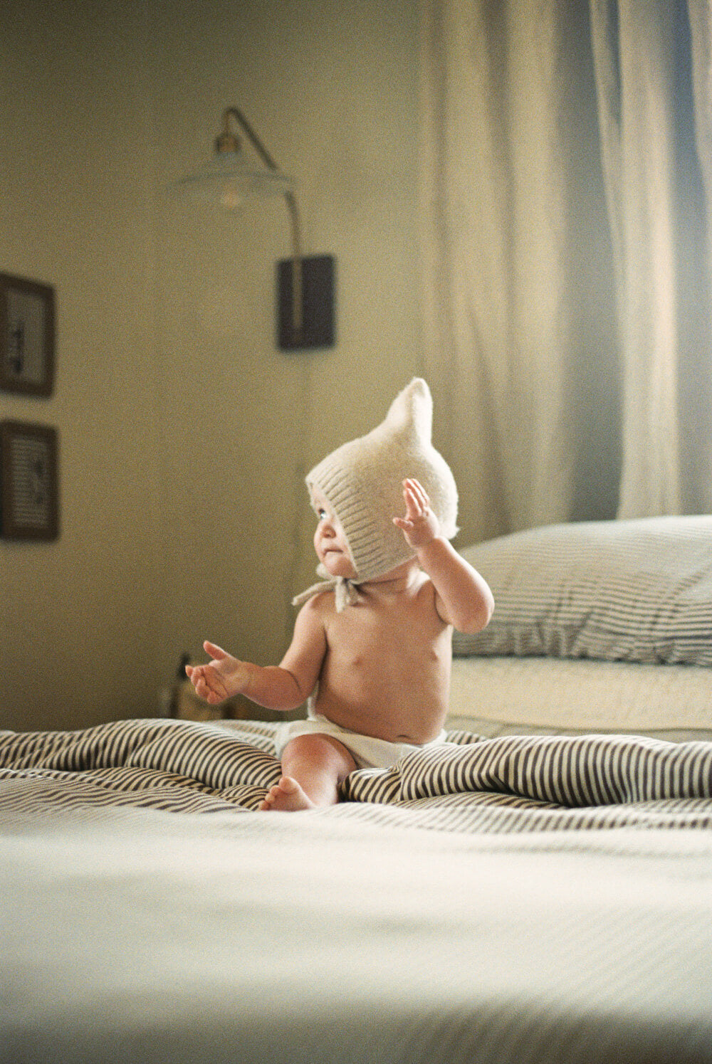 Baby wearing a knitted hat on a bed in a bedroom setting
