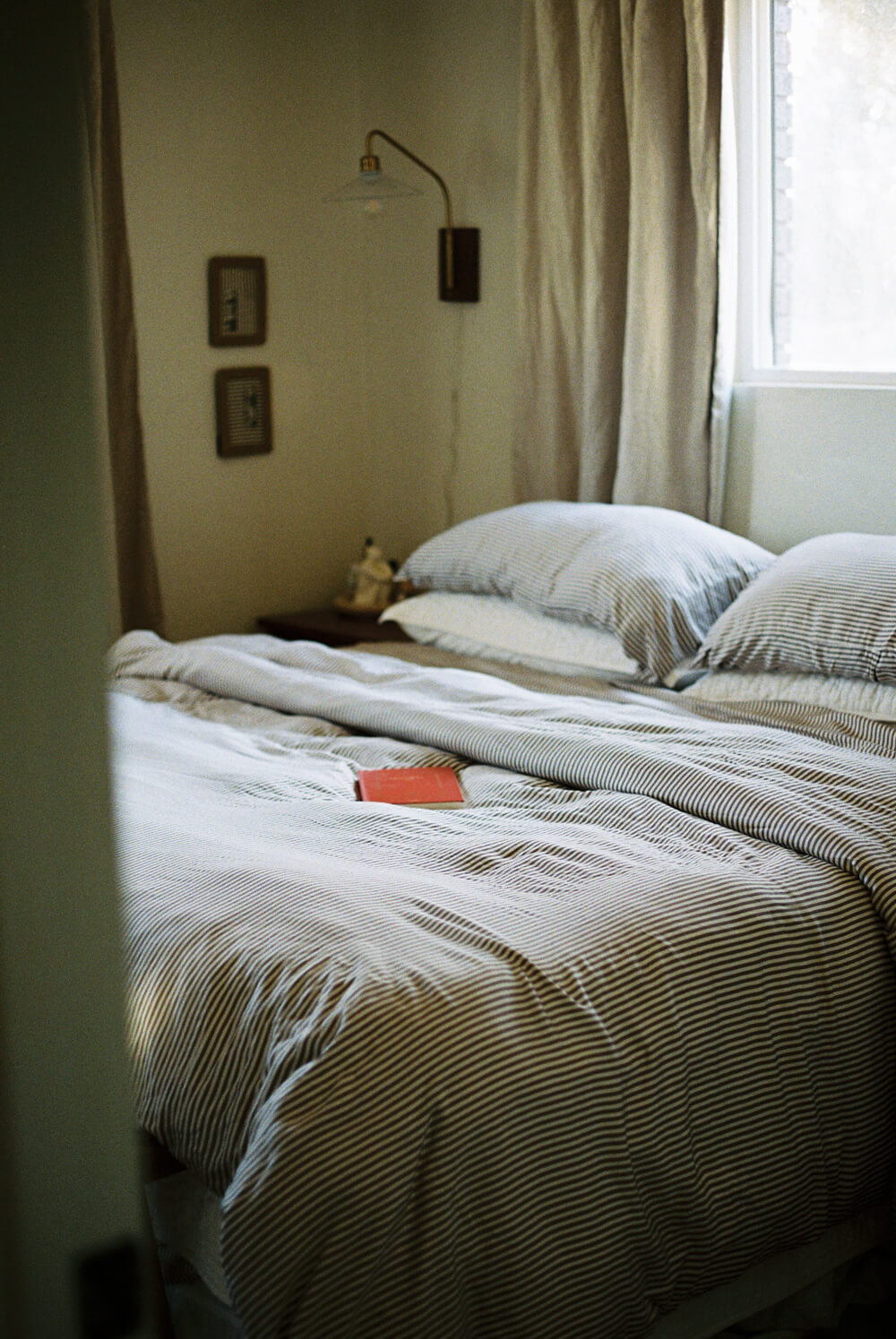 Bedroom with a bed and nightstand, light filtering through curtains.