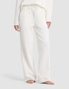 A person is shown barefoot from shoulders to feet against a plain light background, wearing Cozy Earth's Chelsea Pant—a pair of loose-fitting, white drawstring lounge pants—with a matching long-sleeve top.|Color:Bone