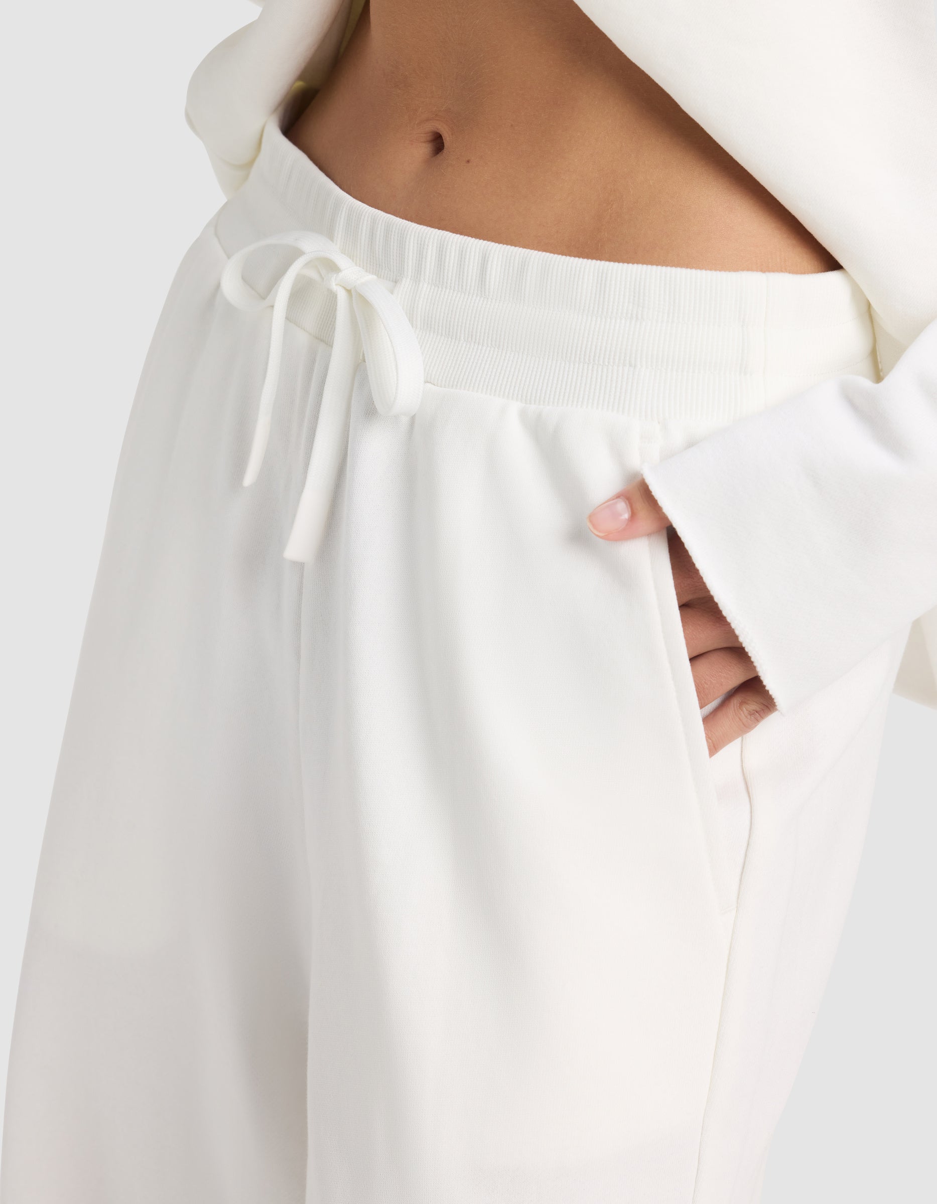 A person wearing Cozy Earth’s Chelsea Pant, featuring a drawstring waist, in white with a matching top and one hand in the pocket.