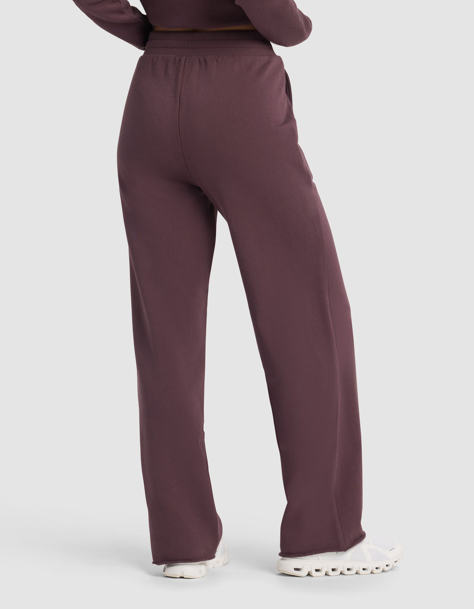 A person is shown from the back wearing Cozy Earth's Chelsea Pant in maroon, a loose-fitting, high-waisted style, paired with white sneakers and arms at their sides.